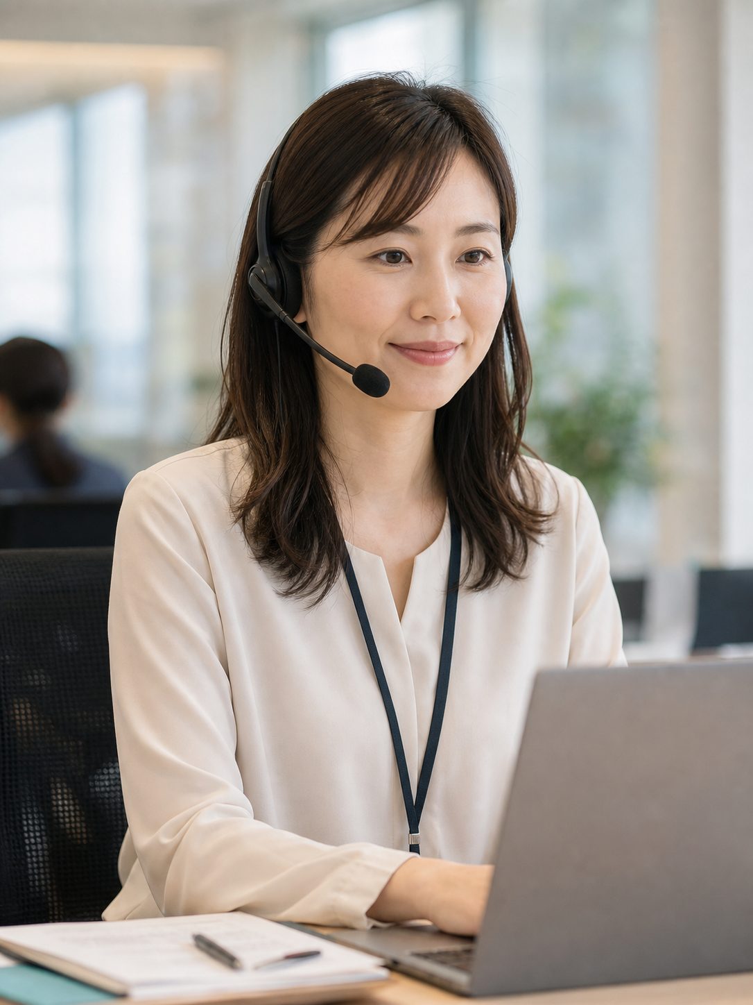 30代女性 カスタマーサポート担当がヘッドセットを付けて笑顔で対応している